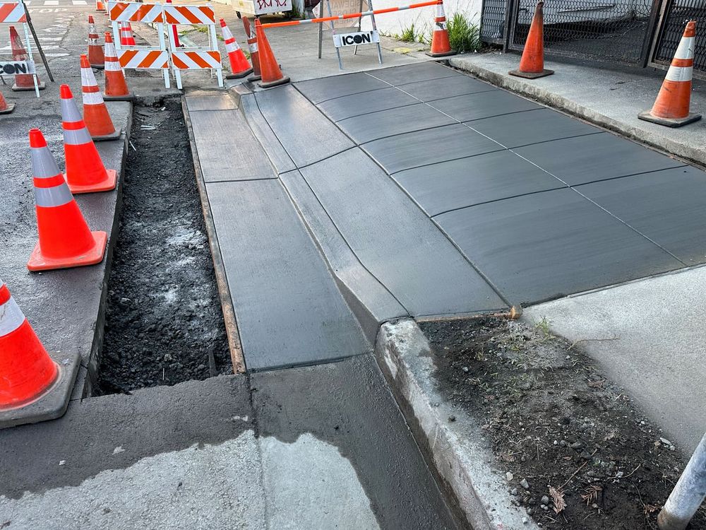 New concrete sidewalk and curb ramp with traffic cones around it